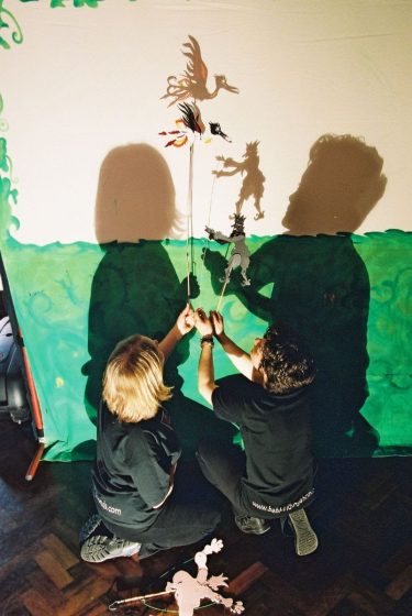 puppeteers holding shadow puppets on a screen