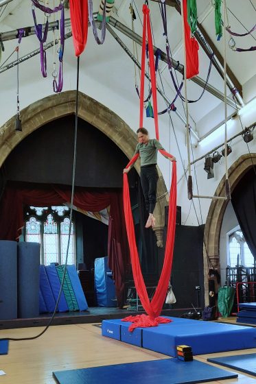 A circus performer in a cross position hanging from red silks