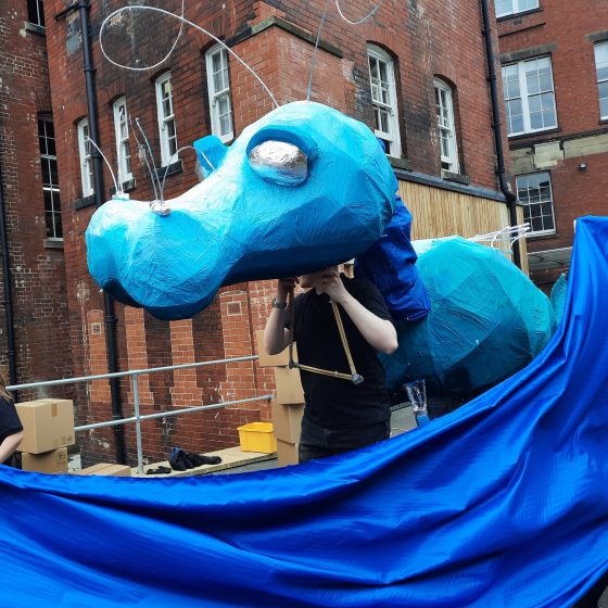 A close up of a giant blue water dragon puppet behind a sea of blue fabric