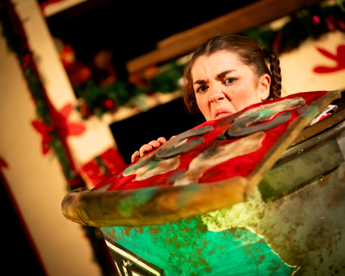 The character naughty meg is looking over a disgusting bin and pulling a face at a grotty piece of oversized pizza