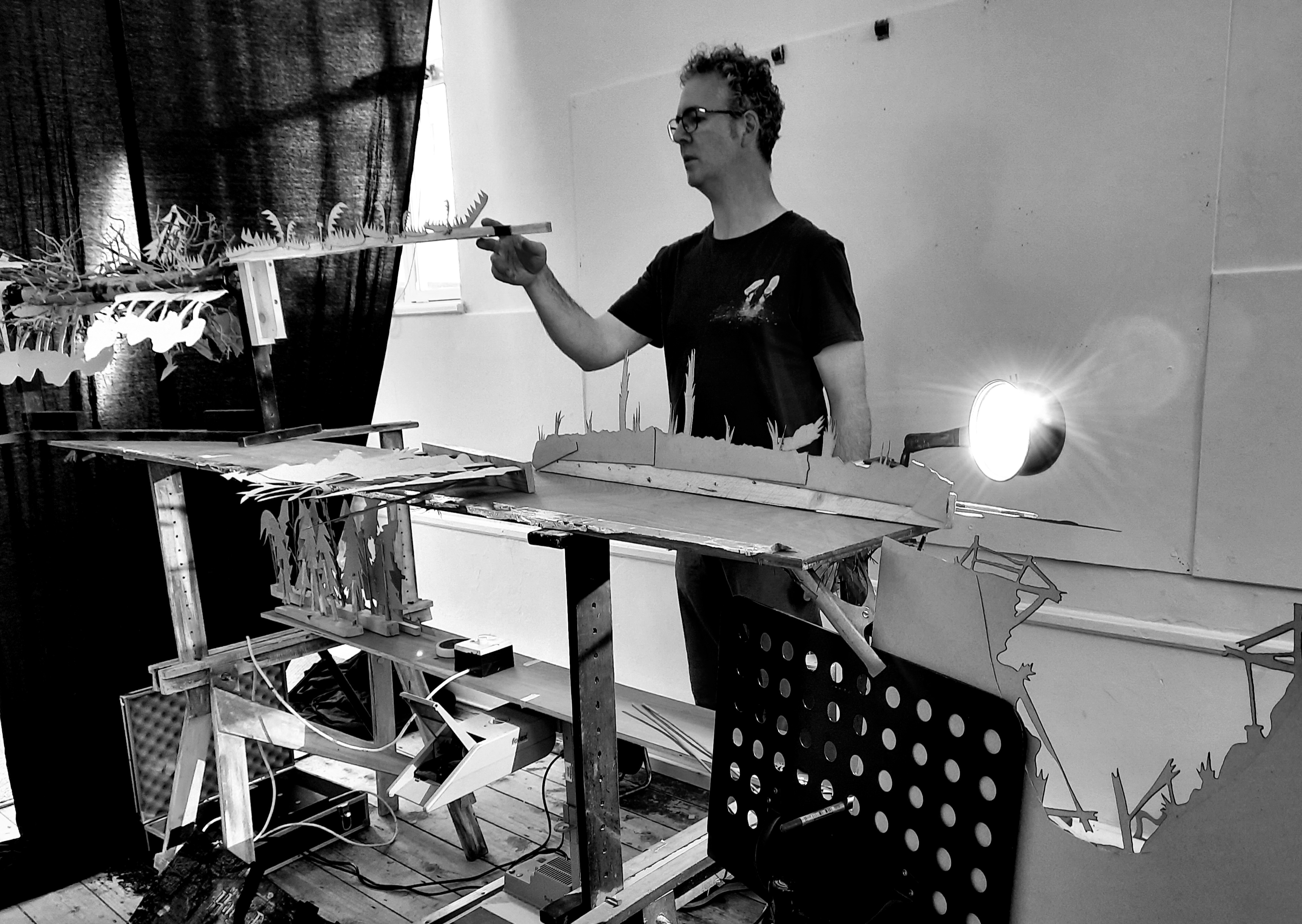 a black and white image of Mark  behind a table operating shadows and lights