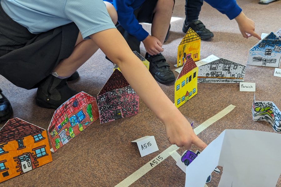 Two school children are crouched low ponting at their drawings of little paper houses