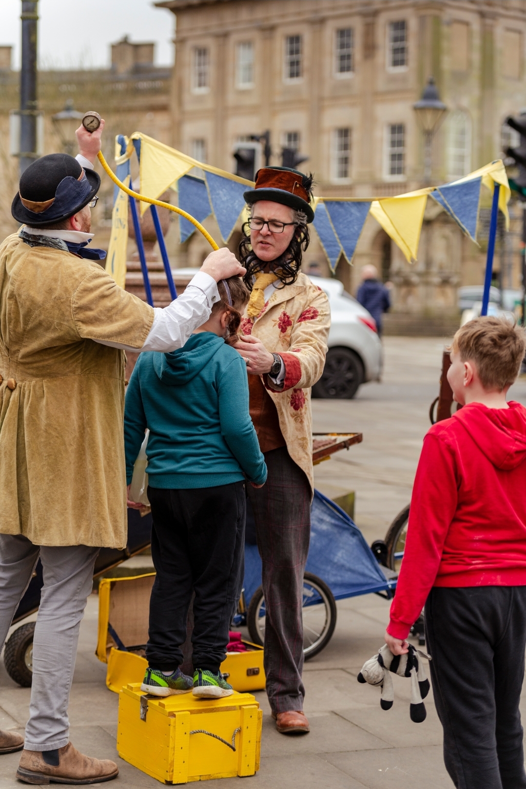 Two men dressed in victorian outfits are looking over a small child trying to work out how to cure them