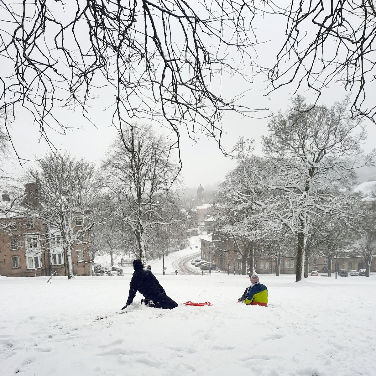 two children sit on a snowy slope looking down at the town