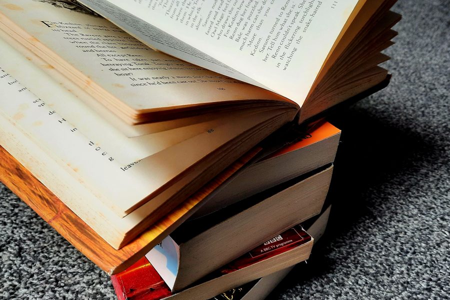 a pile of books are stacked on a carpet. The top book is open and the pages fan out