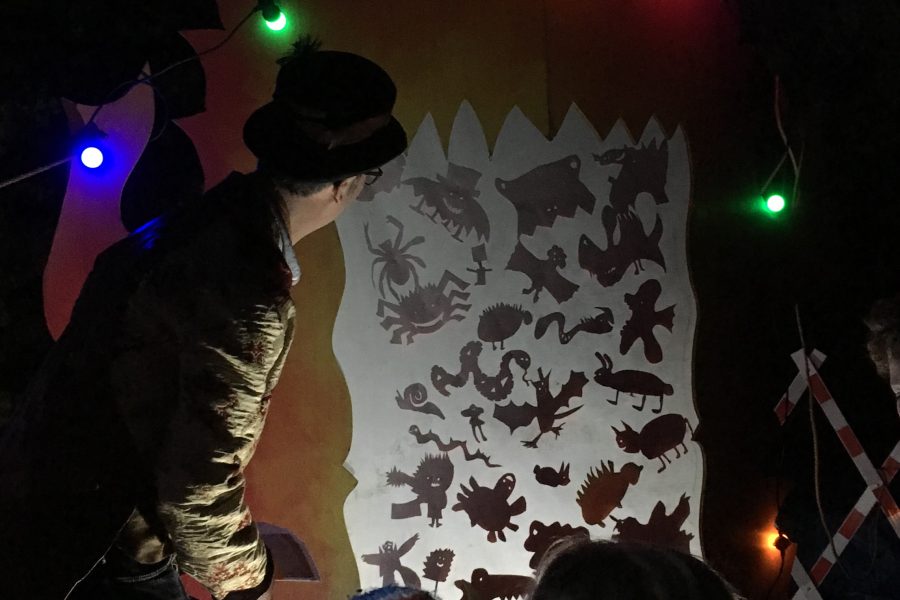 A costume character shows two small children an illuminated shaodw wall full of characters
