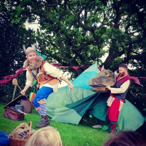 Two male actors tell a story about a dragon. One actor looks like they are running while the other actor holds the head of a large dragon puppet.