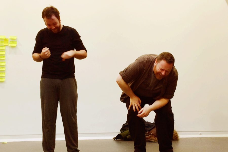 Two male actors are improvising a scene and are laughing, one of the actors is doubled up in hysterics.