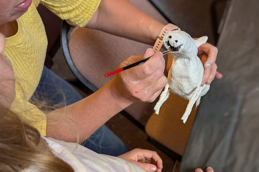 Mother and daughter make a sheep together from mudrock. The view is from above so you see their hands painting their artwork