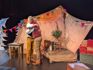 In their show The Night Before The night before Christmas to male characters are hugging on stage. There are presents, bunting and a little chritsmas tree onstage.