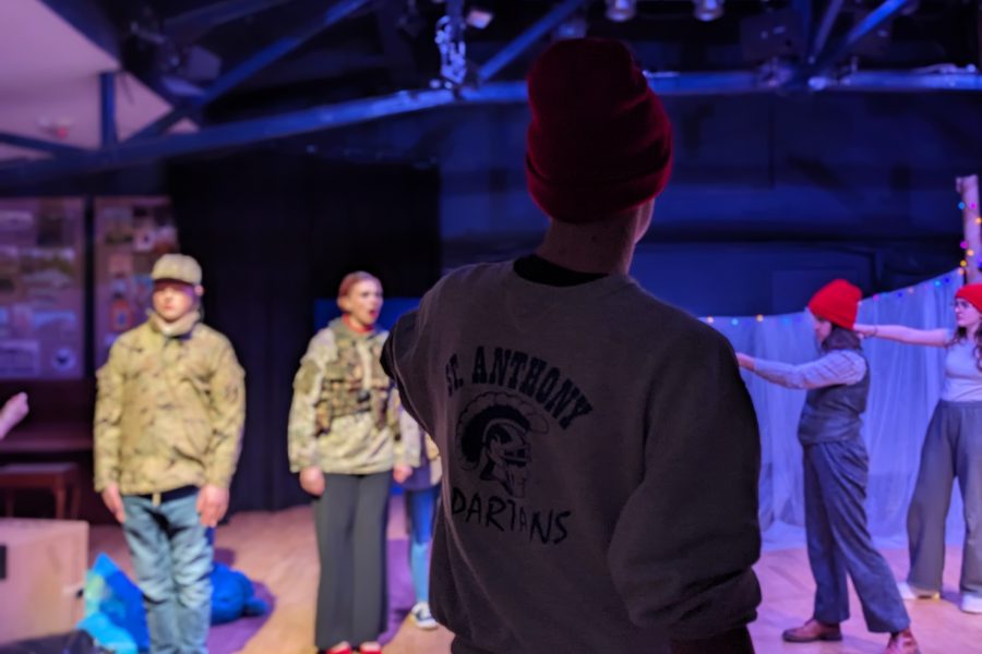 A person has their back to the camera and is looking towards a theatre space. They are wearing a red hat and grey jumper with writing on the back.