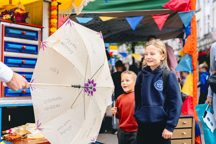 Someone is holding cream umbrella just out of shot. It is open and there are two children looking at it with big smiles on their faces.
