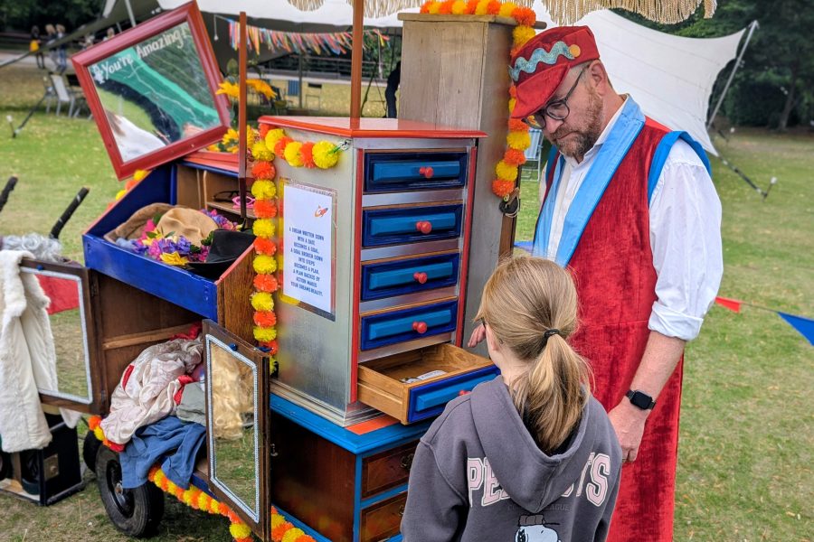 A young girl in a hoodie top with her back to the camera looks into colourful draws with an costumed character in a red hat and over coat.