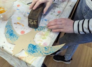 There is a young child using old silk printing blocks to decorate her swift in a family crafts workshop