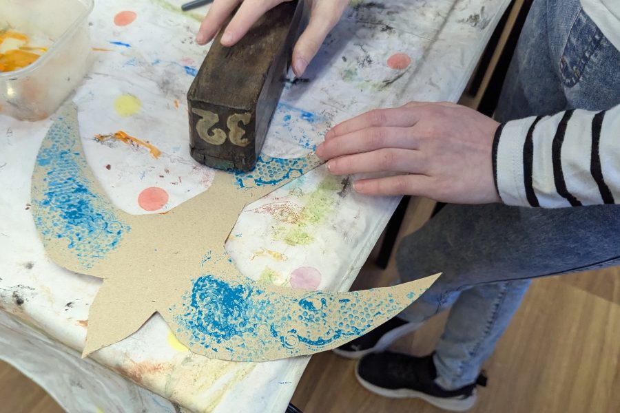 There is a young child using old silk printing blocks to decorate her swift in a family crafts workshop