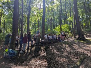 In A beautiful woodland with the sunlight dappled by the leaves, children gather round as their director gives them a team talk before a production.