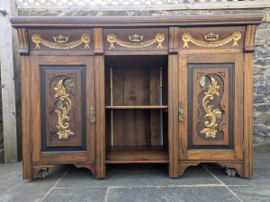 An antique sidboard has been given a make over. It has gold details and black edging and has holes cut in various places as it is a display cabinet
