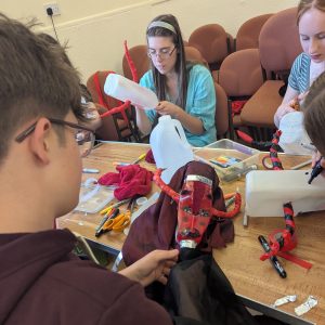 three young people sit around a table making puppets from plastic bottles and found materials