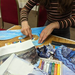 A young person is getting creative and the table is full of craft materials, coloured pastels and magazines cuttings