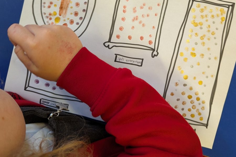 A reception child paints dots into small picture frames that have been drawn on a page