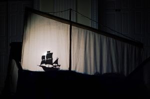 A ships sail becomes a shadow screen and there is a shadow of a pirate ship on the lefthandside