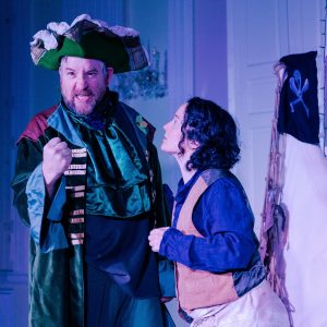 Captain Sprout a pirate dressed in green is looking angry at the camera with a clenched fist. Another pirate is pleading with him