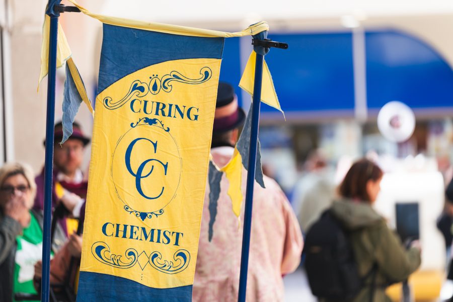 A yellow and blue flag flaps in the wind and the rest of the shot is unfocused. The flag has blue writing and says Curing Chemist