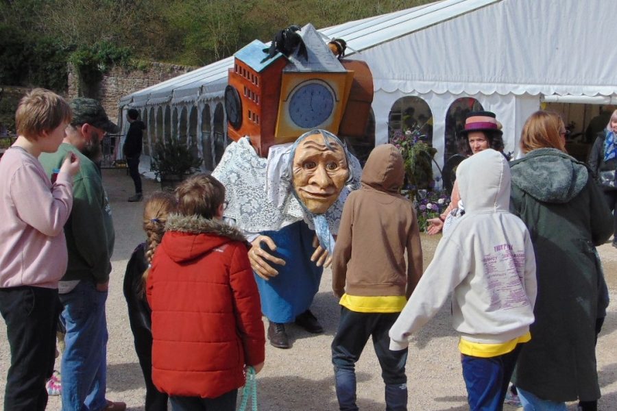 Children gather around a large walkabout puppet, that has been designed like an old lady carrying the world on her back