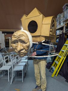 This is a working progress of a very large walkabout puppet. A person stands inside the body section and is hidden by an oversized backpack