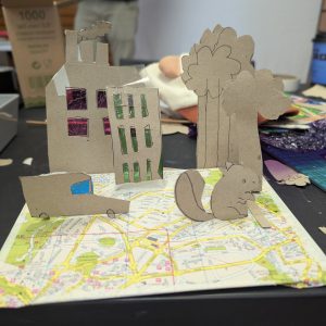 A young person has made a pop up world using an old map as a base and then cardboard for trees, buildings and cars.