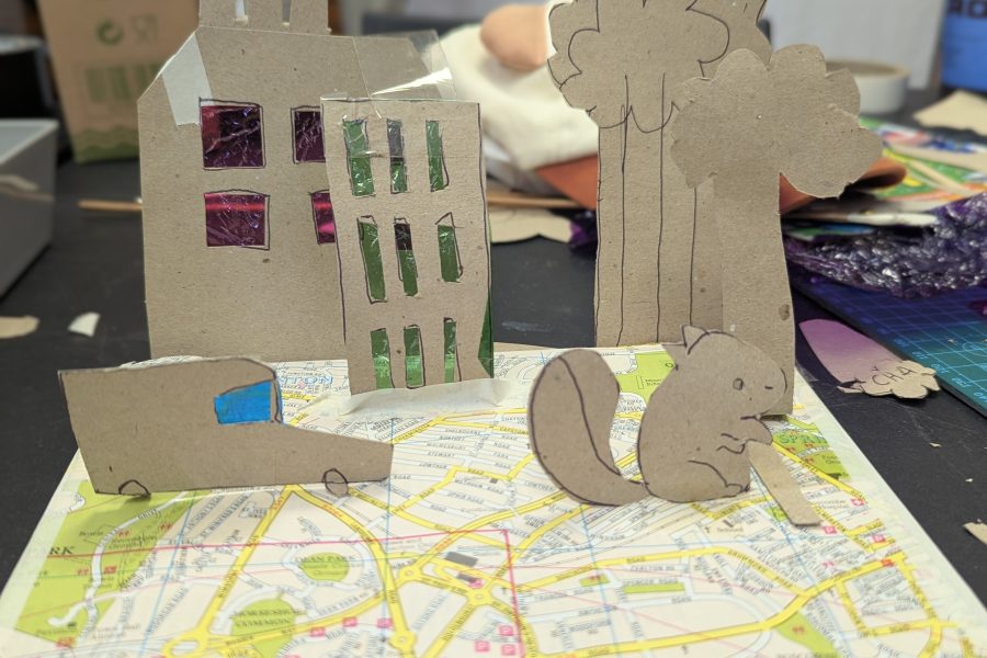 A young person has made a pop up world using an old map as a base and then cardboard for trees, buildings and cars.