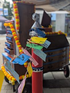 There is the top half of a quirky looking postbox with coloured labels fluttering in the wind that people have written their hopes and dreams on. 