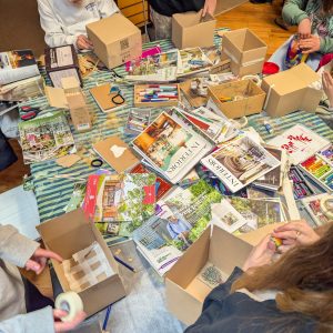 A messy table full of colour and magazines. There are young people sitting around the table creating