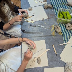 Young people sculpt clay using small tools. The picture is from above and there feels focus on the activity