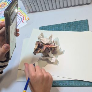 There is a screwed up piece of paper on another piece of paper. Someone is holding their phone with the light on and drawing the shadow of the scrunched up paper