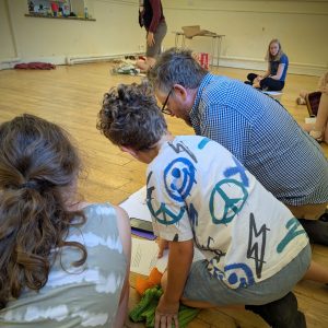 A man and two children gather around a script in a rehearsal of a youth theatre show.