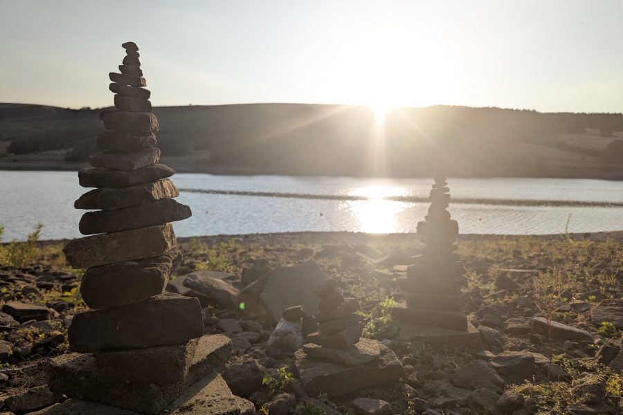 Photo of the eclipse; rocks are carefully stacked one on top of the other on the waters edge of a reservoir, the sun is low in the sky