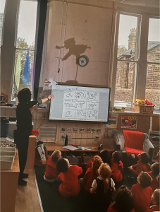 The photographer is stood behind all the children. An artist holds up a shadow puppet to a class of school children. They are all looking up at the shadow it has created