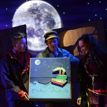 Beneath a big full moon 3 actors watch a small boat sail across the ocean