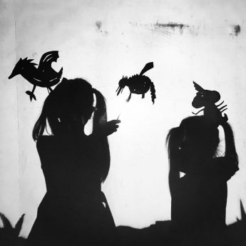 Black and white image of Childrens shilouettes holding shadow puppets
